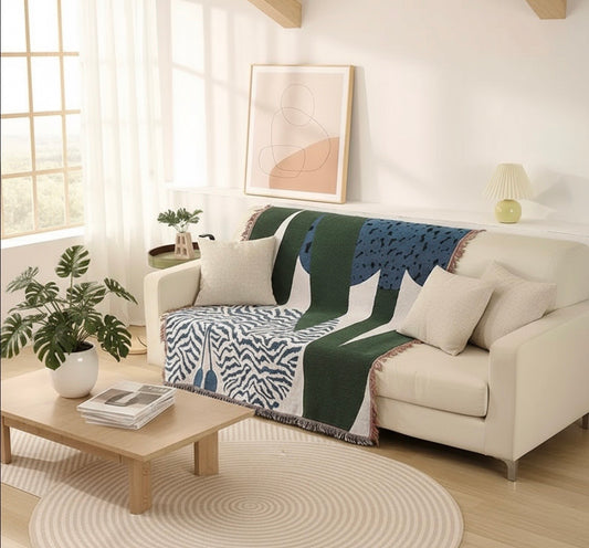 Living room with a white sofa, patterned throw blanket, and a small table with a plant and books.