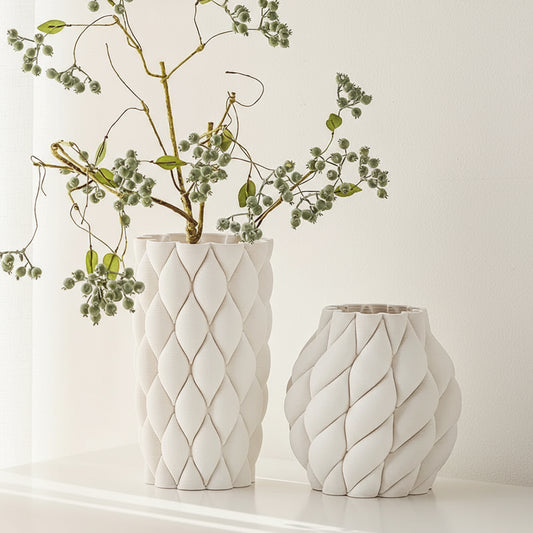 Two white textured vases with decorative patterns on a light background, one holding green branches.