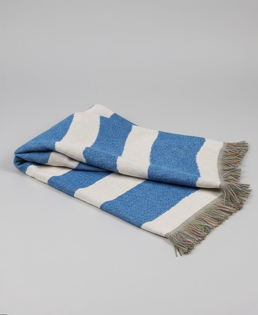 Blue and white striped blanket with fringed edges on a gray background
