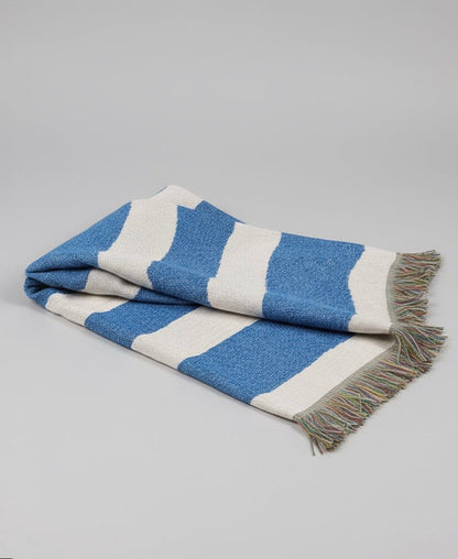 Blue and white striped blanket with fringed edges on a gray background