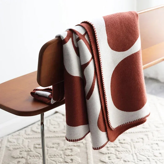 Brown and white patterned blanket draped over a wooden chair on a light-colored floor.