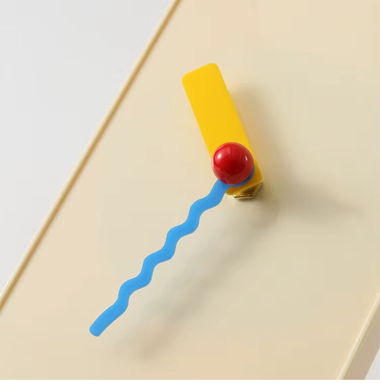 White modern clock with a red ball and blue wavy line on a beige surface