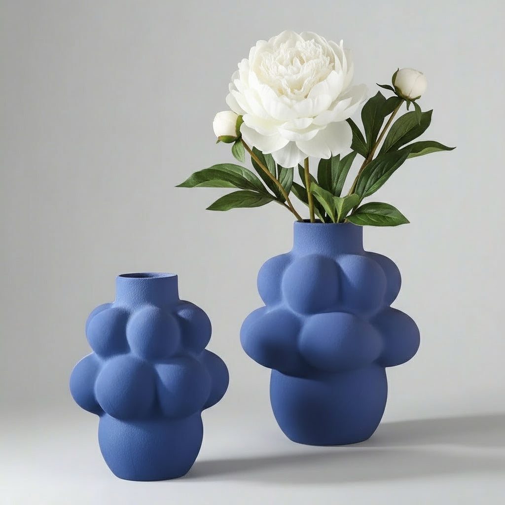 Two blue bubble-shaped vases with a white flower on a gray background