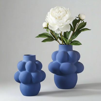 Two blue bubble-shaped vases with a white flower on a gray background