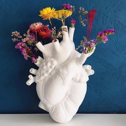 White anatomical heart-shaped vase with colorful flowers against a blue wall.