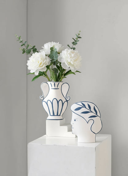 Decorative vase with flowers and a unique head-shaped container on a white surface against a beige wall.