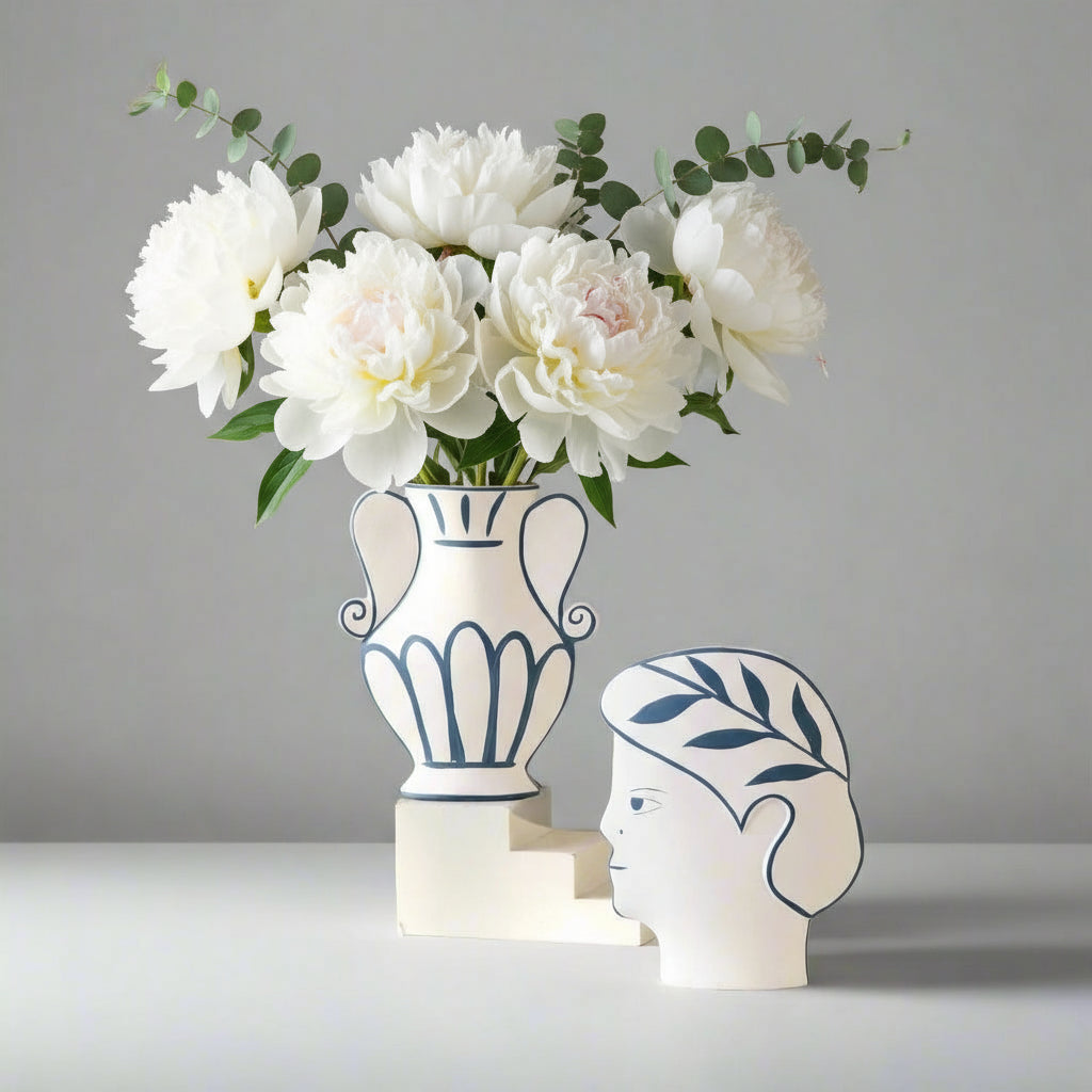 Decorative vase with flowers and a unique head-shaped container on a white surface against a beige wall.