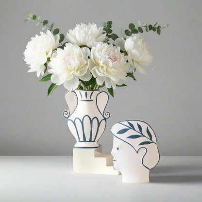 Decorative vase with flowers and a unique head-shaped container on a white surface against a beige wall.