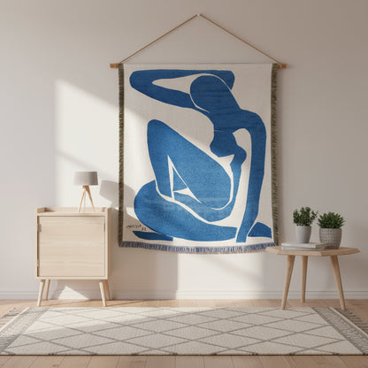 Textile art piece with blue and white abstract design of a sitting figure, hanging on a wall.