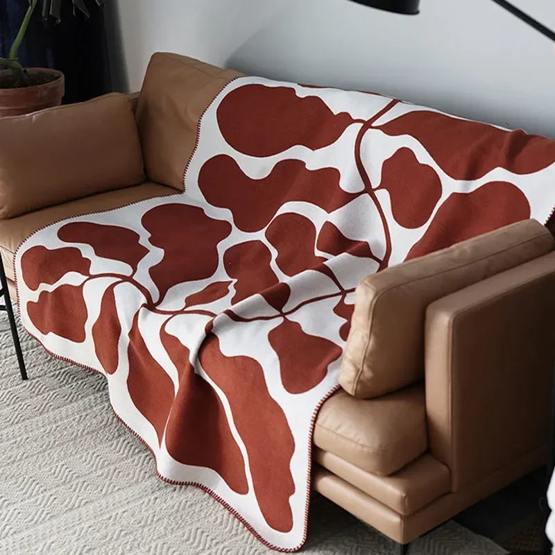 Brown and white patterned blanket draped over a brown sofa in a living room.