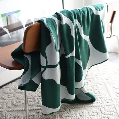 Green and white patterned blanket draped over a chair in a room with a rug and table.