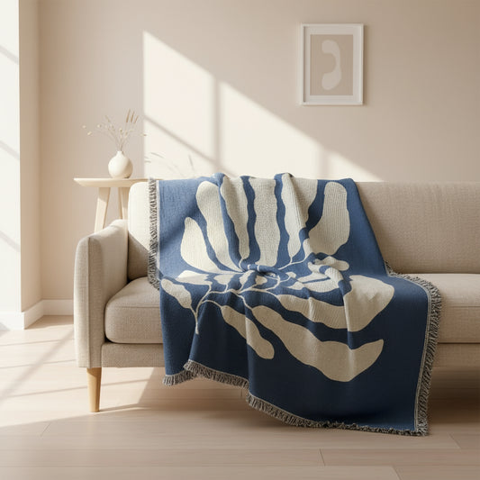 Blue and white leaf-patterned blanket held by a person against a plain wall.