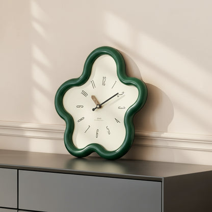 Decorative wall clock with a green frame on a gray surface against a white wall.