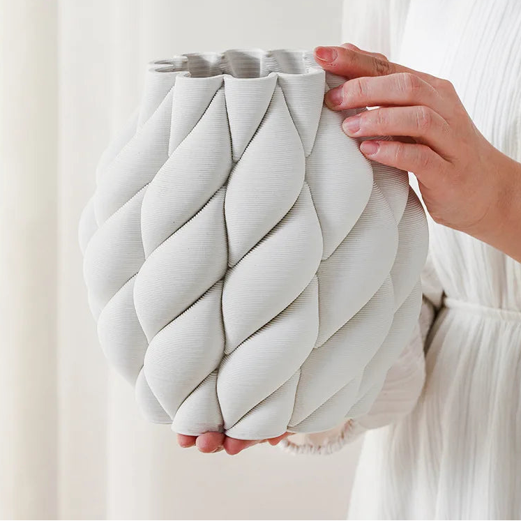 Person holding a braided white ceramic vase against a plain background