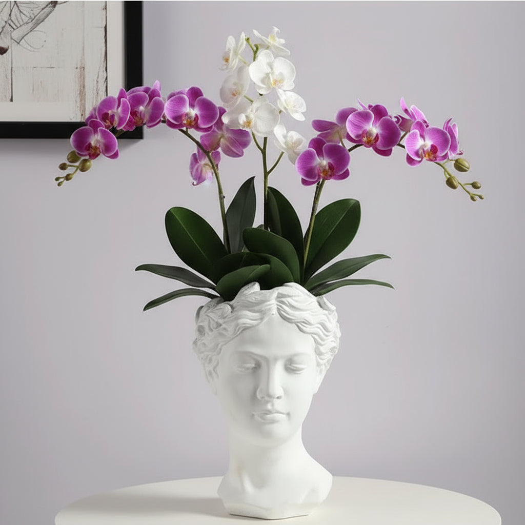 White and purple orchids in a decorative vase shaped like a classical bust on a light gray background.