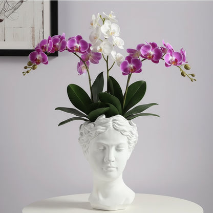 White and purple orchids in a decorative vase shaped like a classical bust on a light gray background.